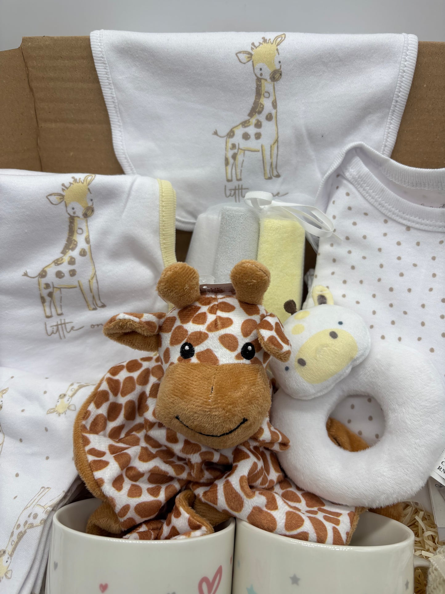 Giraffe baby clothes, comforter and rattle arranged in the gift box