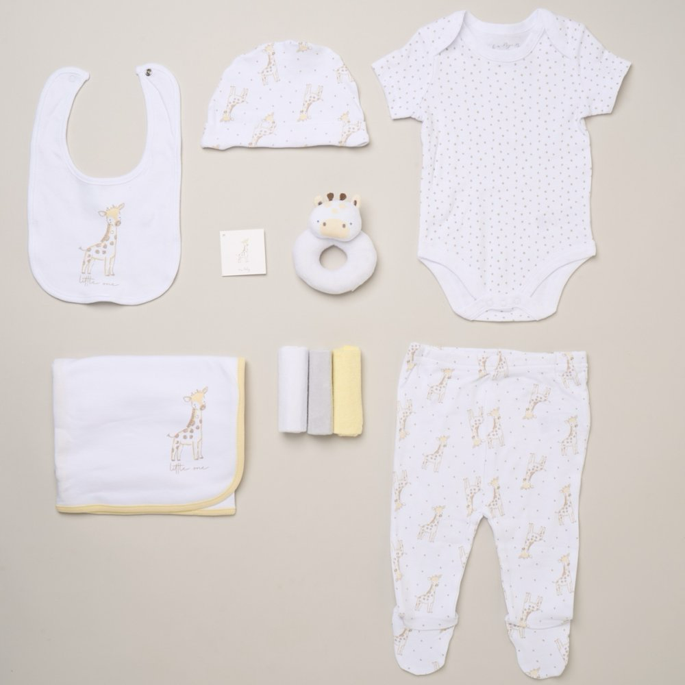Giraffe-print baby clothing set laid flat with bib, hat, spotted bodysuit, footed trousers, blanket, ring rattle and washcloths
