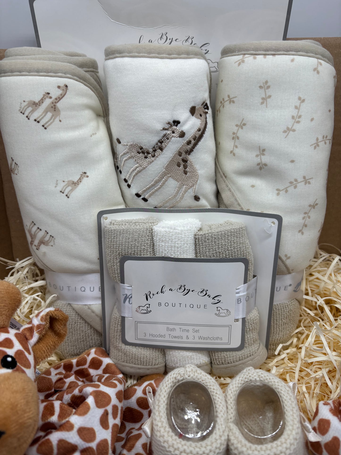 Three neutral giraffe-print hooded baby towels with a washcloth set and cream booties in a gift box