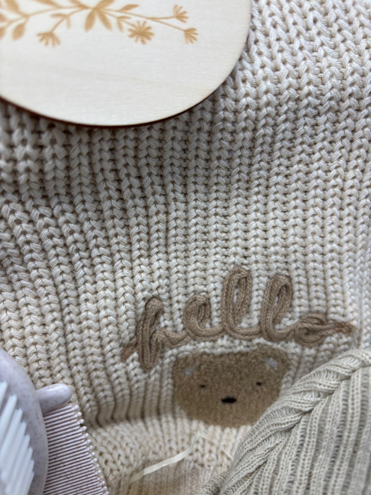 Close-up of the cream knitted baby jumper with Hello embroidery and a teddy face