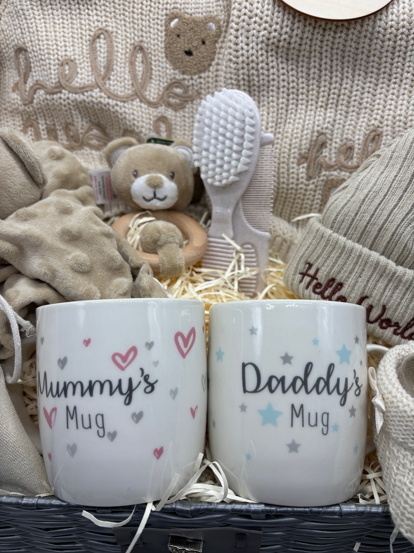 Mummy and Daddy mugs with teddy rattle and baby brush in front of cream Hello World knitwear